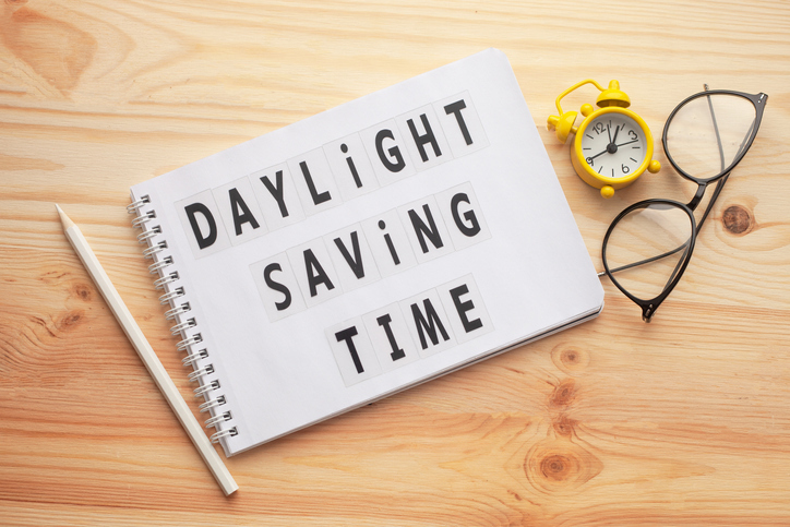 Daylight saving time, notepad with text and retro alarm clock on wooden table.