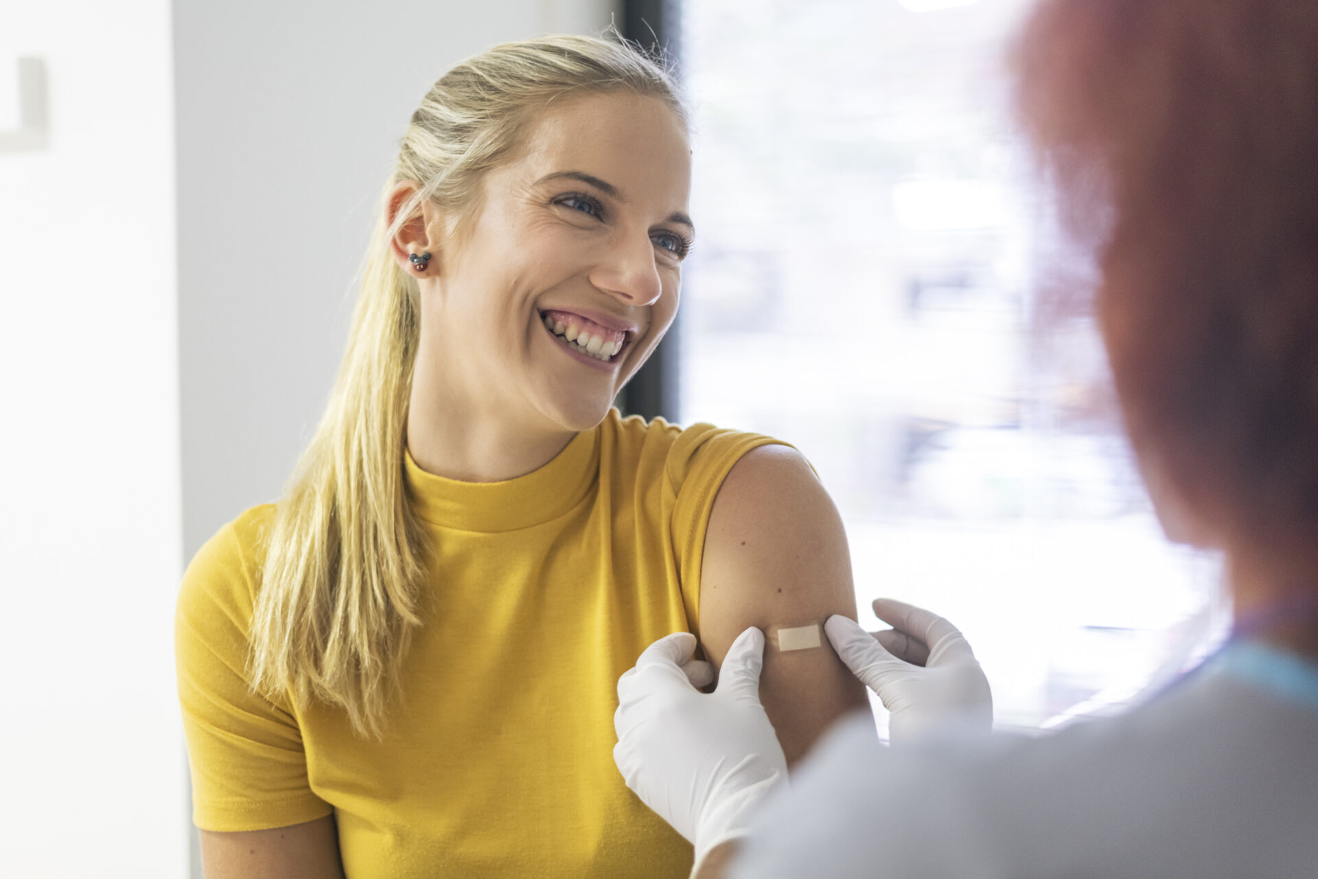 A healthcare worker applies a bandage to a smiling patients arm. The patient has just received the flu vaccine and she appears relieved.